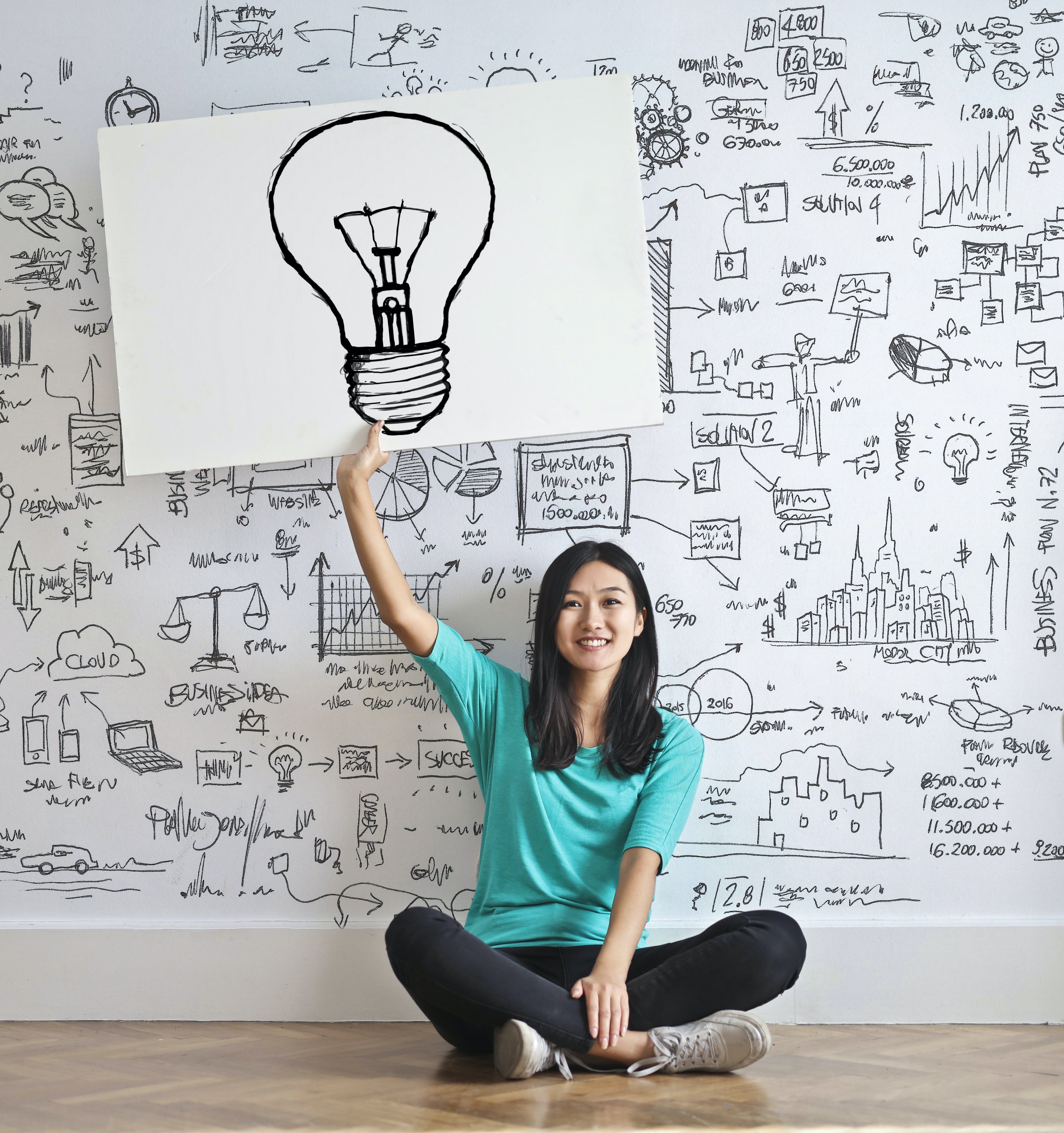 A woman sat before a wall, which is covered in ideas and sketches.
